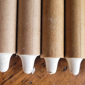 May include: Close-up of seven brown cardboard tubes with white tips. The tubes are arranged horizontally and are all the same size.