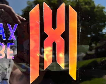 Puede incluir: Una pegatina de vinilo iridiscente roja, naranja y amarilla con un diseño estilizado "XI". La pegatina está en una ventana de coche negra.