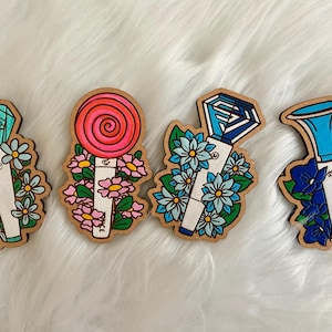 May include: Four wooden fan light stick cutouts with floral accents. The designs include a teal gem, a red lollipop, a blue gem, and a blue horn shape. Each cutout is surrounded by flowers in various colors.