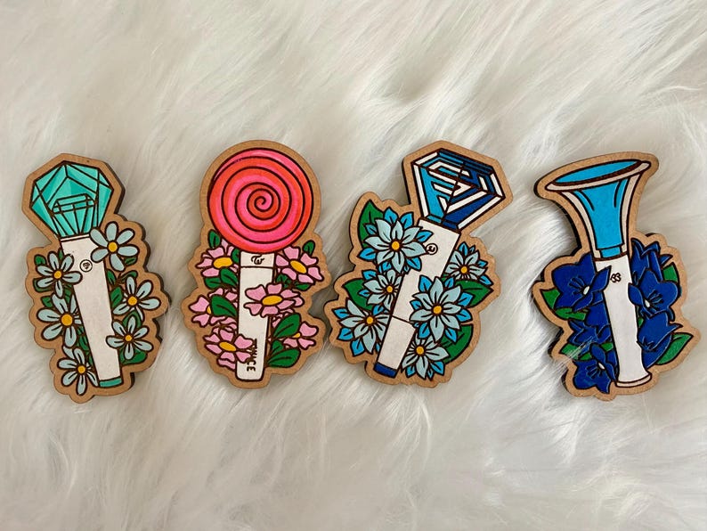 May include: Four wooden fan light stick cutouts with floral accents. The designs include a teal gem, a red lollipop, a blue gem, and a blue horn shape. Each cutout is surrounded by flowers in various colors.