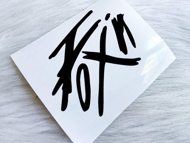 Puede incluir: Una calcoman&iacute;a cuadrada blanca con un dise&ntilde;o gr&aacute;fico negro audaz que se asemeja a una caligraf&iacute;a estilizada dibujada a mano o a trazos de pincel abstractos. Las marcas negras est&aacute;n centradas sobre la superficie blanca, lisa y plana.
