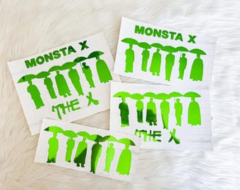 Puede incluir: Cuatro pegatinas de vinilo blanco con un diseño verde. Cada pegatina presenta el texto "MONSTA X" sobre una fila de figuras estilizadas que sostienen paraguas. El texto "THE X" está debajo.