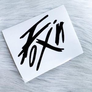 Puede incluir: Una calcoman&iacute;a rectangular blanca que presenta el texto negro "FOX" escrito en una fuente de estilo pincelada, audaz, dentada y estilizada. Las letras est&aacute;n interconectadas con l&iacute;neas n&iacute;tidas y angulares, creando un dise&ntilde;o gr&aacute;fico din&aacute;mico.