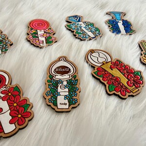 May include: Wooden pins with various designs, including a lollipop, a diamond, and a compass, each surrounded by floral accents. The pins are painted in bright colors and have a natural wood border.