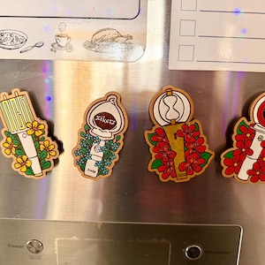 May include: Four wooden magnets with unique designs. One magnet features a yellow and white design with yellow flowers. Another has a white design with the text "xikers" and blue flowers. The other two have red flowers.