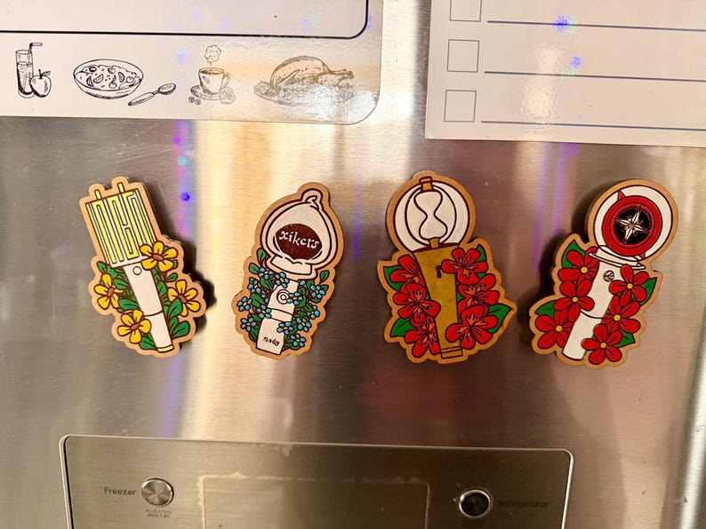 May include: Four wooden magnets with unique designs. One magnet features a yellow and white design with yellow flowers. Another has a white design with the text "xikers" and blue flowers. The other two have red flowers.