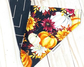 May include: Reversible pet bandana featuring a black and white chevron pattern on one side and a fall-themed pumpkin and floral print on the other. The bandana showcases orange, white, and yellow pumpkins and flowers against a black background.