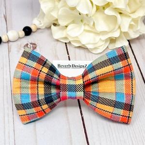 May include: A plaid bow tie with orange, blue, black, and beige colors. The bow tie is tied and ready to wear. BeverlyDesignZ is printed on a white tag.