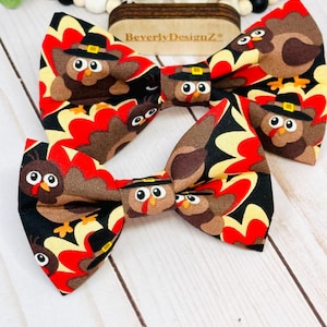 May include: Two Thanksgiving-themed bow ties. The bow ties feature a repeating pattern of cartoon turkeys wearing pilgrim hats, set against a backdrop of red, black, and yellow shapes. The text "BeverlyDesignZ" is visible on a wooden tag.