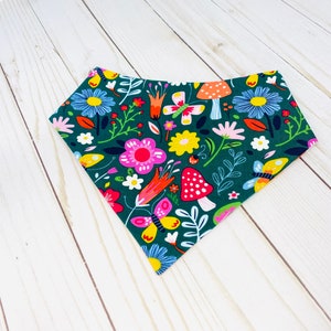 May include: A green bandana with a floral and mushroom print. The print features pink, yellow, red, and white flowers, mushrooms, and butterflies.