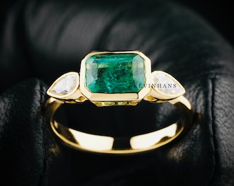 May include: A gold ring with a large emerald green gemstone and two smaller pear-shaped diamonds.