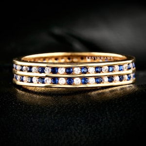 Könnte beinhalten: Ein Goldring mit zwei Reihen blauer Saphire und weißen Diamanten. Der Ring ist in einer polierten Goldband gefasst.