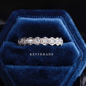 May include: A silver band ring with a row of hexagonal-shaped diamonds set in a bezel setting. The ring is displayed in a blue velvet ring box with the text "KEVINHANS" printed on the bottom.