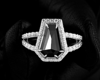 May include: A silver ring with a black diamond set in a coffin-shaped setting. The diamond is surrounded by smaller diamonds.