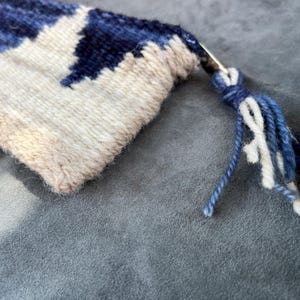 May include: A close-up of a woven tapestry with a blue and white geometric pattern. The tapestry has a fringe on one end.