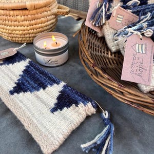 May include: A woven tapestry with a blue and white geometric pattern and a blue tassel. The tapestry is labeled "woven with hope".