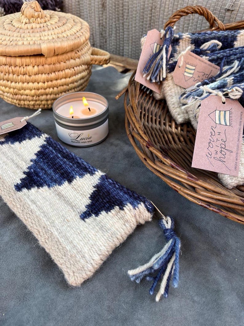 May include: A woven tapestry with a blue and white geometric pattern and a blue tassel. The tapestry is labeled "woven with hope".