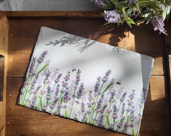 May include: A white slate coaster with a painted design of lavender flowers and bees. The coaster is on a wooden surface.