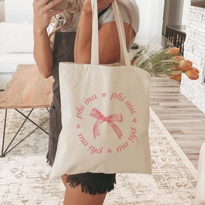 May include: A white canvas tote bag with a pink ribbon and the text "phi mu" repeated around the circle.