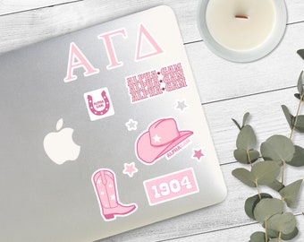 May include: A silver laptop with pink stickers. The stickers include a horseshoe with the text "Alpha Gam", a cowboy hat with a star, a pair of cowboy boots, a rectangle with the text "1904", and the text "Alpha Gam" repeated three times. The laptop also has a pink sticker with the Greek letters "ΑΓΔ".