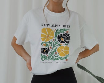 May include: White t-shirt with a floral design and the text "Kappa Alpha Theta, Established 1870, Greencastle, IN".