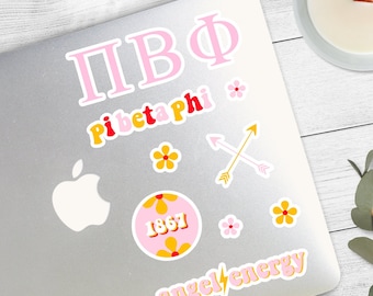 May include: A silver laptop with a variety of stickers. The stickers are pink, yellow, and red. The stickers include the letters "ПВФ", "Pi Beta Phi", a flower, a circle with the number "1867", two crossed arrows, and the words "angel energy".