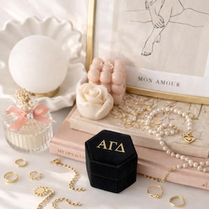 May include: A collection of jewelry and decorative items. Includes gold rings, necklaces, a black velvet ring box with gold lettering, a perfume bottle, candles, and a framed print that reads "MON AMOUR".