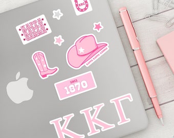 May include: A laptop computer with pink and white stickers. The stickers include a horseshoe with the letters KKG, a cowboy hat with a star, a boot with stars, a star, a text box with the words "Kappa Kappa Gamma", a text box with the words "Since 1870", and a large text box with the letters "KKG".