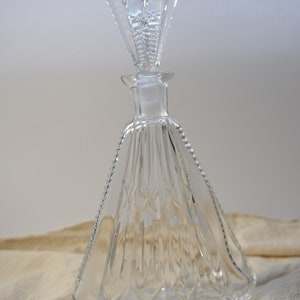 May include: A clear glass decanter with a faceted design and a crystal stopper. The decanter has a wide base and a narrow neck.