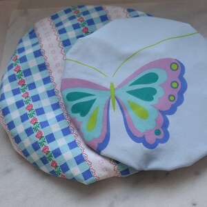 May include: Two fabric bowl covers. One is blue with a white and pink butterfly design. The other is blue and white gingham with a white and pink floral border.