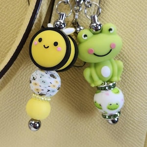 May include: A yellow and black bee charm with a white and yellow bee patterned bead and a yellow bead. A green frog charm with a white and green frog patterned bead.