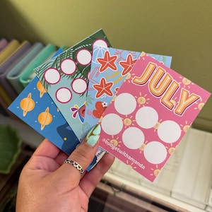May include: Four colorful printable habit tracker cards with a summer theme. The cards feature a blue card with planets, a green card with palm trees, a blue card with starfish, and a pink card with the word "JULY" and suns. Each card has blank circles for tracking habits.