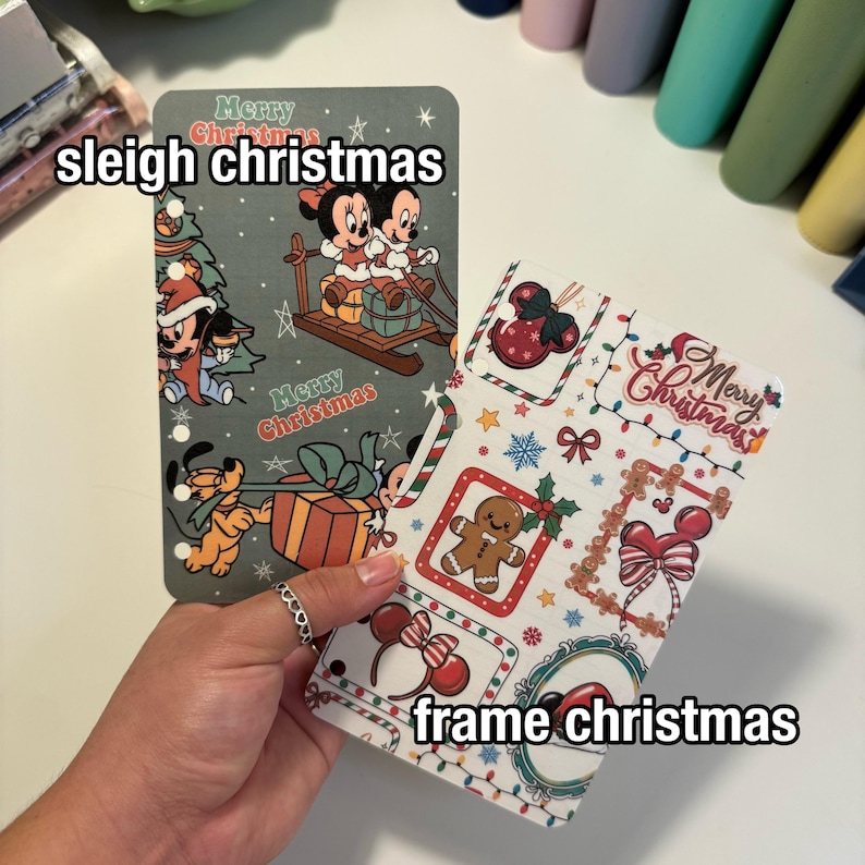 Op de afbeelding: Twee plannerinzetstukken met kerstthema. E&eacute;n toont Mickey en Minnie Mouse op een slee, met de tekst "sleigh christmas". De andere heeft een peperkoekmannetje en andere feestelijke elementen, met de tekst "frame christmas".