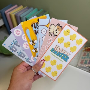 May include: A set of colorful stickers featuring various designs, including a cat, bees, a swirl pattern, milk cartons, and a happy Easter message with yellow chicks. The stickers are on a white background and have a handwritten hashtag #budgetwithamanda.