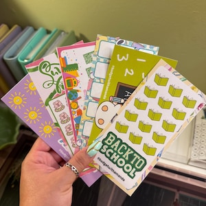 May include: A set of six colorful back to school themed planner stickers. The stickers feature a variety of designs, including a chalkboard, a backpack, a globe, a book, and a sun. The stickers are all decorated with bright colors and fun patterns. The stickers are perfect for adding a touch of personality to your planner or journal.