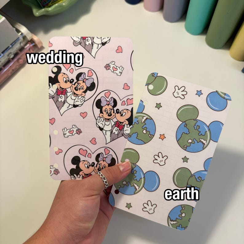 Op de afbeelding: Twee decoratieve kaarten met Mickey en Minnie Mouse. E&eacute;n kaart heeft een roze achtergrond met Mickey en Minnie in harten, het woord "wedding" staat op de kaart. De andere kaart heeft een witte achtergrond met Mickey Mouse-vormige globes en het woord "earth".