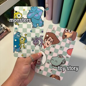 Op de afbeelding: Twee decoratieve kaarten met stripfiguren. E&eacute;n kaart heeft het woord "monsters" en toont Sully en Mike Wazowski. De andere kaart heeft de woorden "toy story" en toont Woody en Rex. Beide kaarten hebben een geruite achtergrond.
