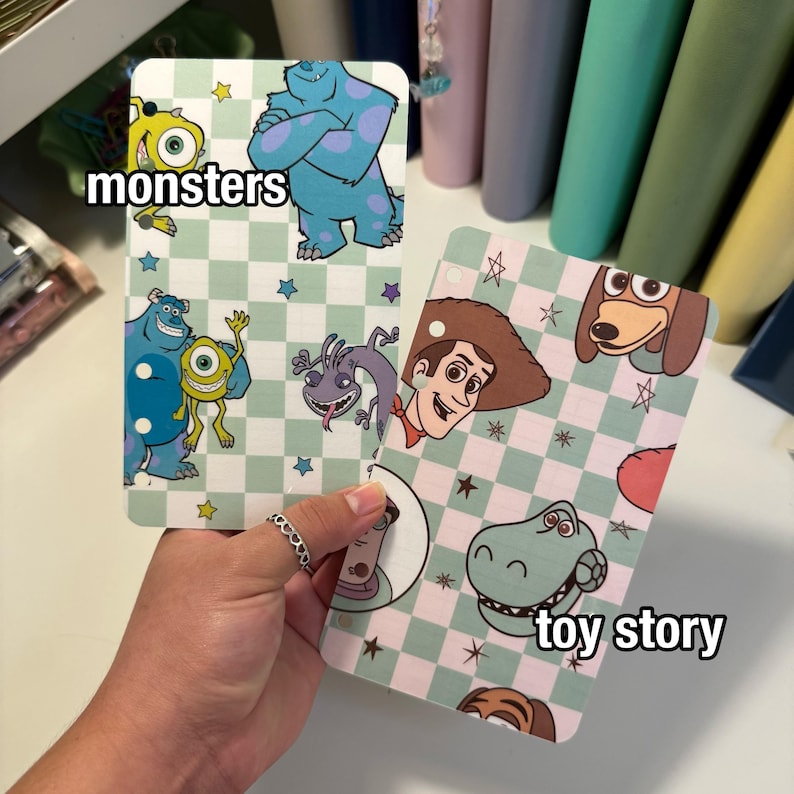 Op de afbeelding: Twee decoratieve kaarten met stripfiguren. E&eacute;n kaart heeft het woord "monsters" en toont Sully en Mike Wazowski. De andere kaart heeft de woorden "toy story" en toont Woody en Rex. Beide kaarten hebben een geruite achtergrond.