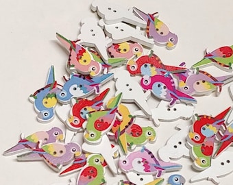 May include: A collection of colorful wooden parrot buttons. The buttons are painted with various colors and patterns, including red, blue, green, yellow, and purple. The buttons are all in the shape of a parrot with a beak and wings.