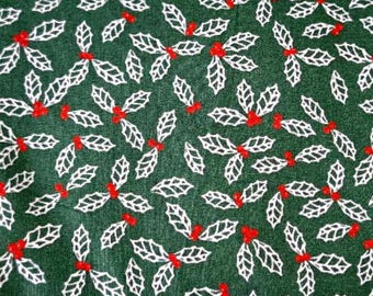 May include: A roll of green fabric with a repeating pattern of white holly leaves and red berries. The fabric is wrapped in clear plastic. A metal ruler with inch measurements is at the bottom.