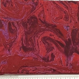 May include: Red fabric with a marbled pattern. The fabric is approximately 12.7 cm wide.
