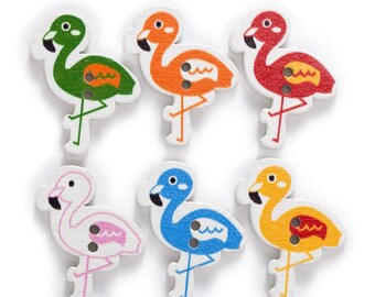May include: Six wooden buttons shaped like flamingos in different colors: green, orange, red, white, blue, and yellow. Each button has a black eye and a white beak.