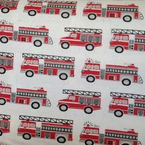 May include: A repeating pattern of red and grey fire engines on a white background. The fire engines have black ladders and wheels. The pattern is evenly spaced across the fabric.