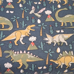 May include: A navy blue fabric with a repeating pattern of cartoon dinosaurs, volcanoes, palm trees, and cacti. The dinosaurs are in shades of yellow and green. White eggs are scattered throughout the design.