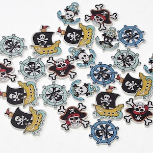 May include: A collection of 20 wooden pirate-themed buttons with various designs, including skulls, crossbones, ships, anchors, and steering wheels. The buttons are painted in bright colors, including red, blue, yellow, and black.