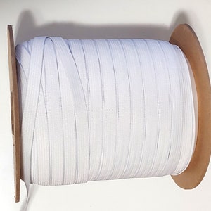 May include: A spool of white elastic cord wound around a brown cardboard core.