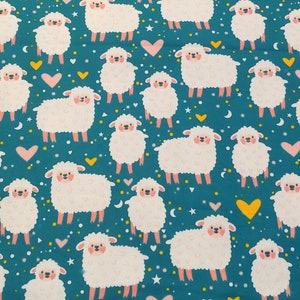 May include: A teal fabric with a repeating pattern of white fluffy sheep with pink cheeks. The sheep are scattered across the fabric with small white stars and yellow and pink hearts.