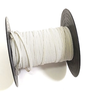 May include: A spool of white elastic cord with a black plastic bobbin. The cord is wound tightly around the bobbin.