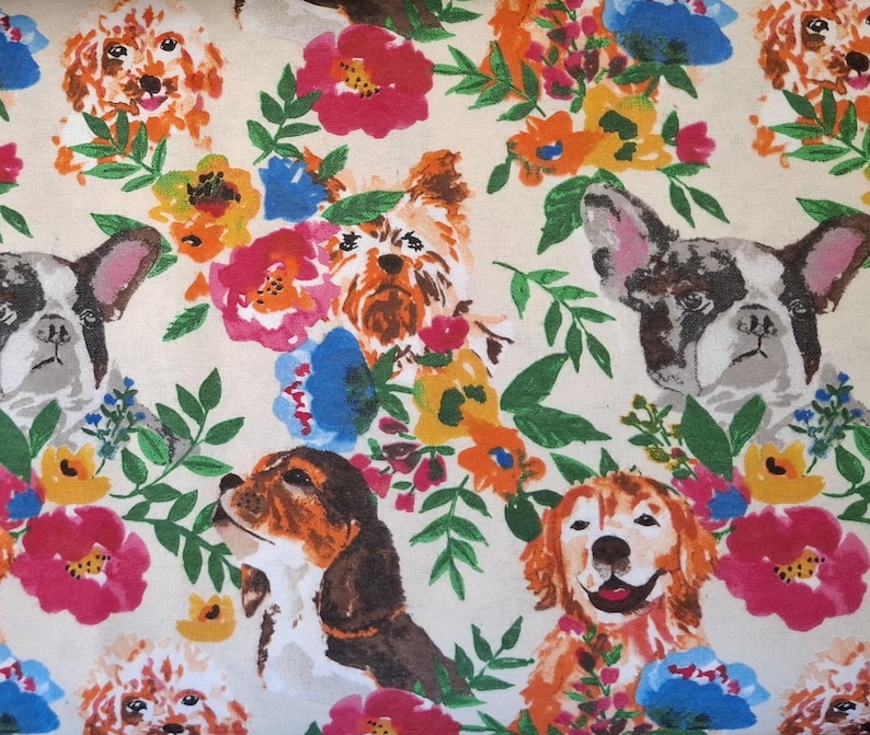 May include: A cream-colored fabric featuring a repeating pattern of various dog breeds and colorful flowers. The dogs include a French Bulldog, a Beagle, a Golden Retriever, and a Yorkshire Terrier, surrounded by pink, blue, orange, and yellow flowers.