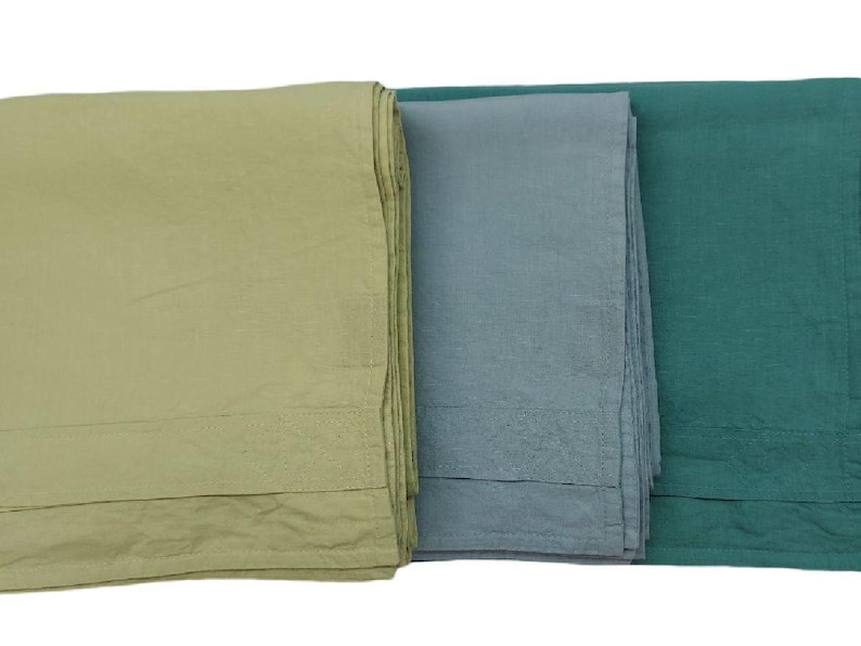 Op de afbeelding: Drie gevouwen linnen textielsoorten in tinten groen, blauwgrijs en blauwgroen. De stoffen zijn opgestapeld en tonen hun textuur en kleurvariaties. De randen zijn netjes gezoomd.